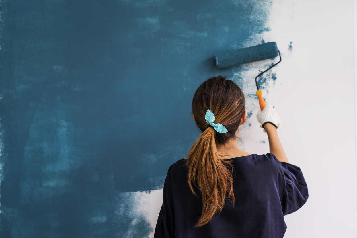 Woman painting dark blue over white walls