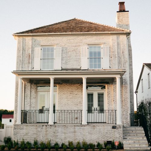 Whitewashed brick home exterior in Avorio White with brown shingles, warm white trim, and black iron railing